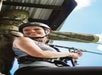 Woman wearing a helmet and harness smiles while secured to ropes at an outdoor adventure or zip lining course.