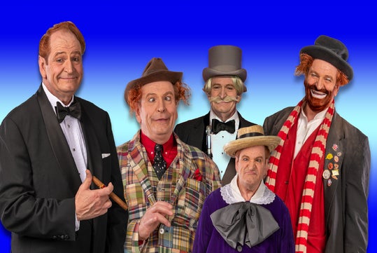 Five men in colorful clown costumes and makeup; one in a tuxedo, others in playful attire with eccentric hats, standing against a blue gradient background.