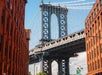 View of the Manhattan Bridge framed by two red-brick buildings on a clear day.