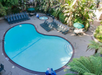Aerial view of a kidney-shaped outdoor swimming pool surrounded by lounge chairs, with a small hot tub nearby, amidst lush greenery.