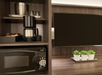 A microwave, coffee maker, mugs, and ice bucket are on shelves next to a flat-screen TV and three small potted plants on a wooden surface.