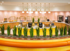 A breakfast buffet counter with various food items, plants along the front, and modern lighting fixtures overhead in a brightly lit dining area.