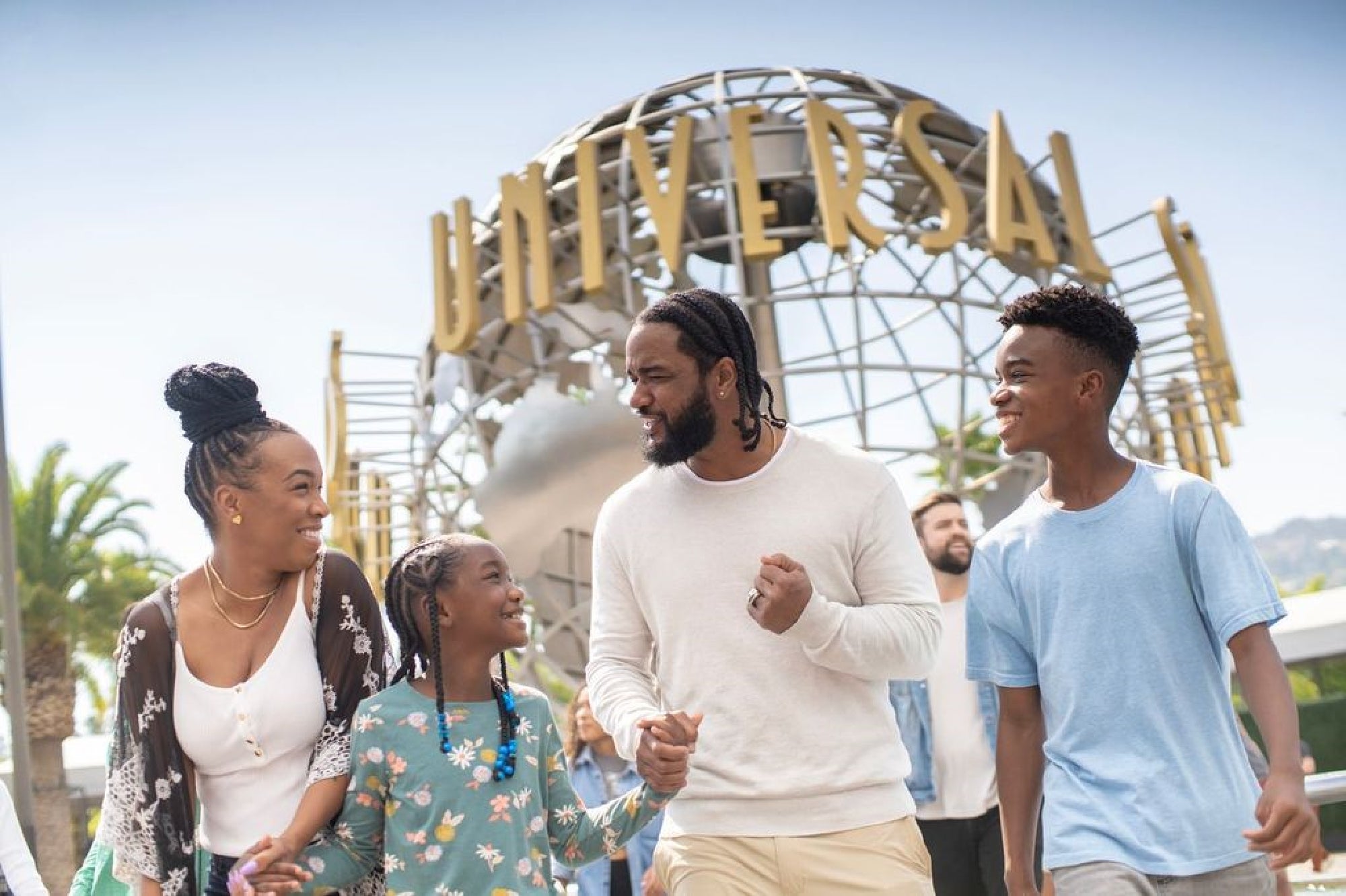 A family of four smiles and walks together in front of the Universal Studios globe landmark on a sunny day.