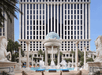 Large hotel with tall windows and central dome structure, surrounded by palm trees and statues, with a pool in the foreground.