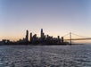 San Francisco skyline at dusk with the Bay Bridge on the right and city buildings silhouetted against the sunset sky, viewed across the water.