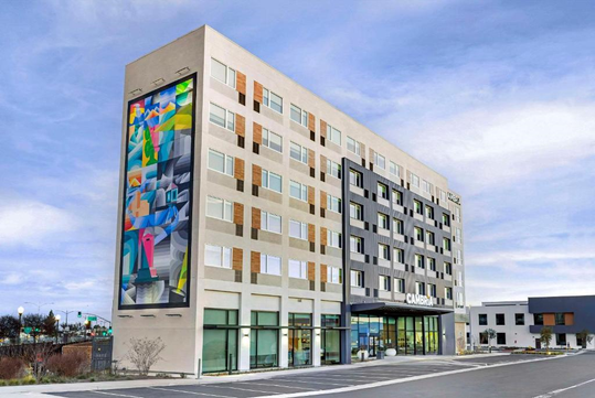 Modern hotel building with colorful mural on the facade, featuring large windows and multiple floors under a clear sky.