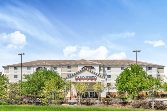 Front view of a three-story hotel with a terracotta roof, surrounded by trees, under a clear blue sky.