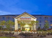 Front view of Candlewood Suites hotel with illuminated signage, surrounded by trees and plants, set against a twilight sky.