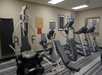 A gym with exercise machines including treadmills, a stationary bike, and a strength training machine on a striped carpeted floor.
