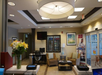 Hotel lobby with seating area, floral arrangement on the desk, computers, a TV, vending machine, and a large ceiling light fixture. Sliding glass entry doors are on the right.