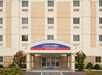 Front view of a Candlewood Suites hotel entrance with beige exterior, arched canopy, and surrounding green shrubs.