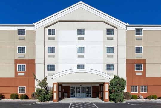 Four-story building with a central archway entrance, cream and brown facade, and parking area in front.