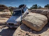 A NAVTEC land cruiser driving through large rocks on a sunny day in Canyonlands National Park.