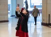 A woman wearing glasses and a red dress takes a photo with her phone inside a spacious, well-lit public building. Other people and a statue are visible in the background.