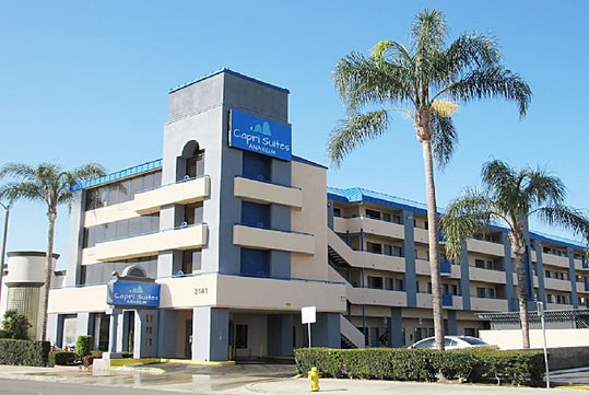 Exterior view of the Capri Suites Anaheim on a sunny day with 3 palm trees in front of it near Los Angeles, California, USA