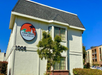 Two-story building with a sloped roof. A sign reads "Carlsbad Village Inn" with a palm tree logo. Visible address number is 1006. There's greenery in front of the building.