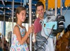 A father and daughter riding a carousel and smiling at Carowinds in Charlotte, North Carolina.