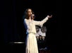 Sally in a white dress singing during a live performance.