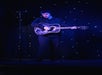A person stands on a stage playing an acoustic guitar under blue lighting, with a microphone stand nearby and a backdrop of small, glowing lights.
