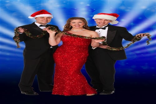 Three people dressed in formal wear and Santa hats pose together, holding a tinsel garland, in front of a blue, festive backdrop.