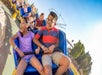 A young boy and girl sitting in a blue seat at the front of a roller coaster on a curve with more kids and parents in the seats behind them.