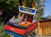 A group of excited riders on the "Rockin' Tug" amusement ride, with their hands raised in joy as the colorful boat tilts and spins in a playful manner.