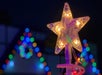 Close-up of a lit star-shaped topper on a Christmas tree with colorful holiday lights blurred in the background.