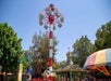 A tall red and white drop ride with the passenger cars sitting at the top and other rides and attraction around it on a sunny day at Castle Park.