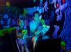 A father and daughter holding laser guns on a dark ride with spooky purple and green decorations all around them.