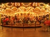 A brightly lit carousel at night, adorned with glowing lights and colorful horses, with blurred figures of people enjoying the ride.