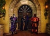 Three costumed figures in a medieval-themed setting: a skeleton in purple armor, a woman in a black gown striking a pose, and a muscular figure in red armor, all standing in front of an ornate wooden door at Castle Park.