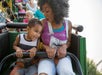 A mother and son laughing and having a good time while riding a small green rollercoaster.