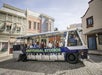 A Universal Studios tour tram with passengers drives through a movie set street lined with colorful buildings and storefronts.