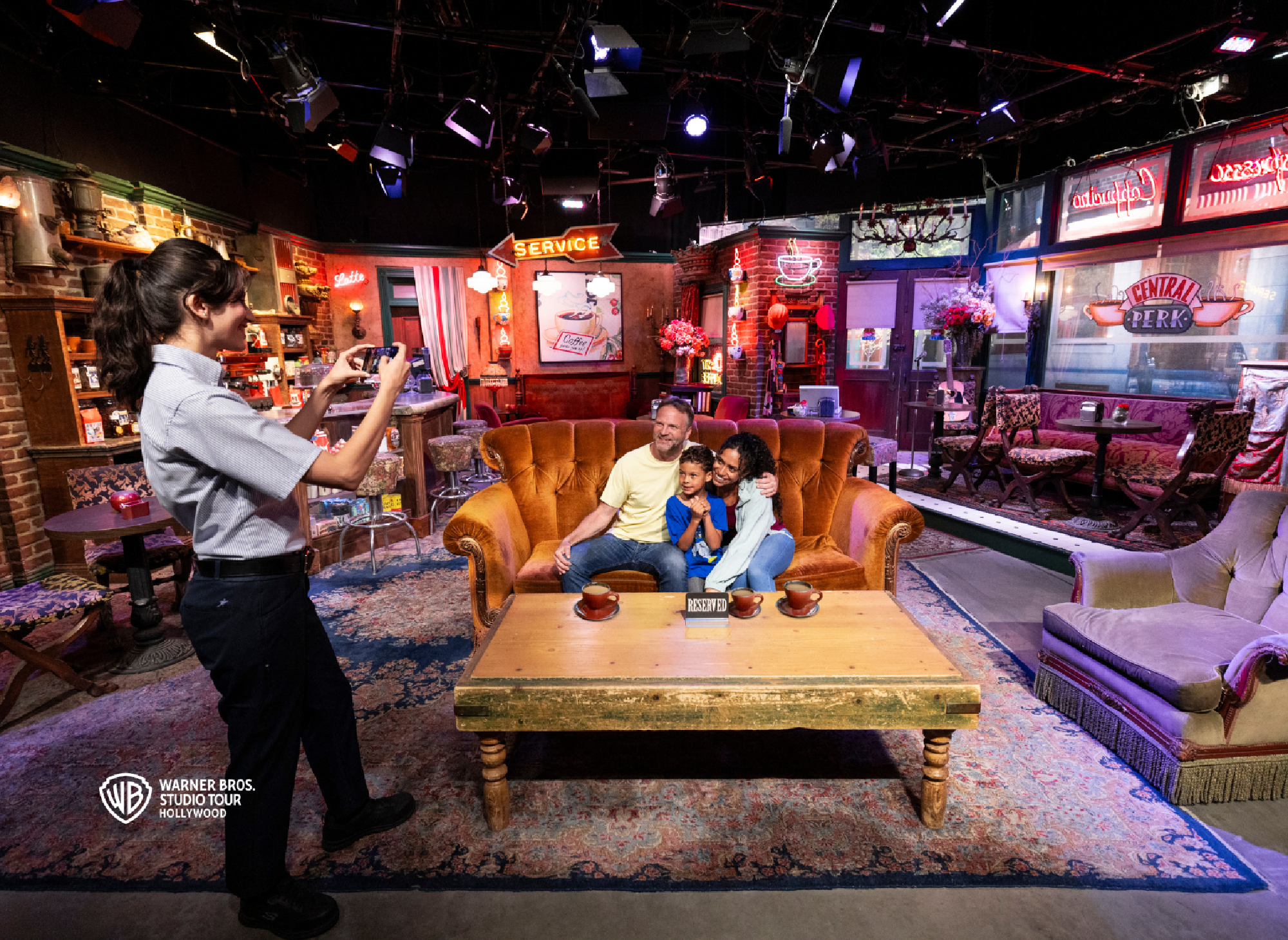 A family poses for a photo on the iconic orange couch set from the TV show "Friends" at the Warner Bros. Studio Tour, while an employee takes their picture.