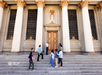 A group of people stand at the steps of a large, ornate building with tall columns and decorative carvings during a Warner Bros. Studio Tour.