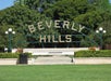 The image shows the iconic Beverly Hills sign in Los Angeles, positioned in a park with trees and greenery surrounding it.
