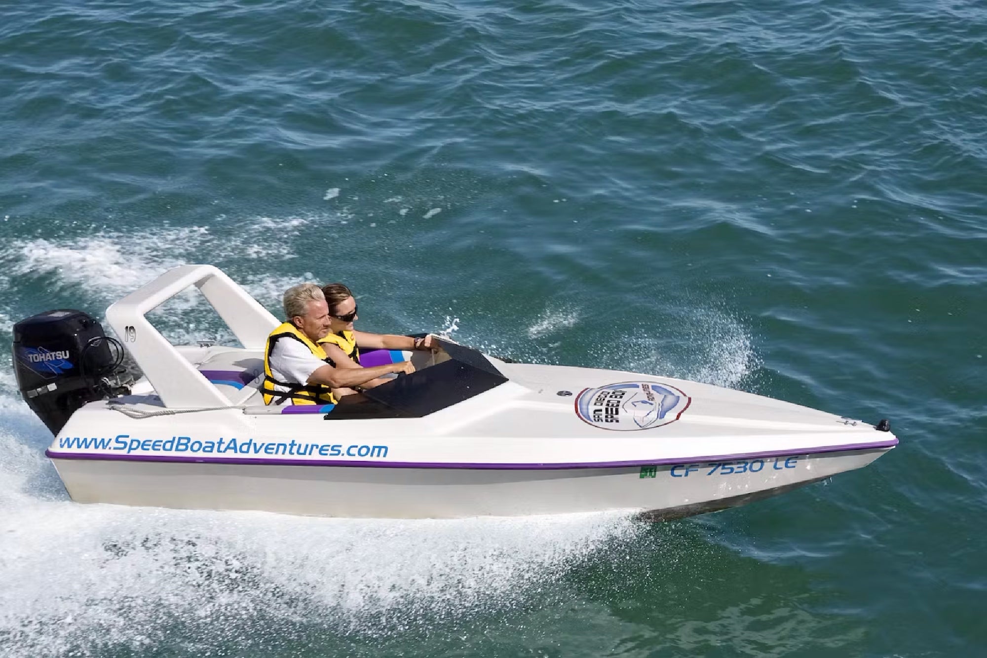 Two passengers steering a speedboat through Charleston Harbor.