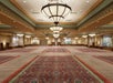 Spacious ballroom with elegant chandeliers, patterned carpets, and large wall art, featuring high ceilings and an open floor.