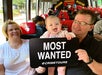 A family with a baby holds a "Most Wanted" sign on a bus with themed decor.