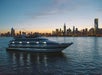 A large cruise ship on the water with the city of Chicago and the sun setting behind it on the Chicago Premier Dinner Cruise on Lake Michigan.