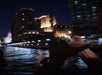 A person takes a photo of illuminated city buildings at night from a waterfront location, using a smartphone.