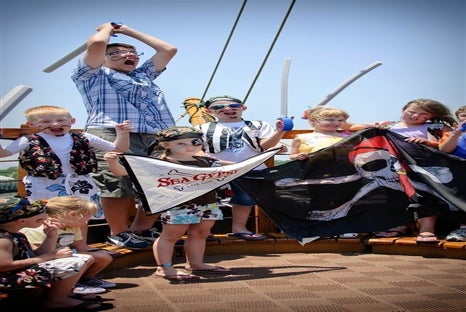 Several kids with face paint and other pirate accessories holding pirate flags on Sea Gypsy pirate ship on a sunny day.