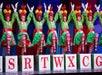 The Radio City Rockets dressed at rag dolls with red hair and green dresses with one of their legs up on red and white letter blocks.