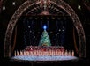 Wide shot of the Christmas Spectacular Starring the Radio City Rockettes with the performers in a line on stage in front of a giant Christmas tree.