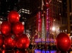 The exterior of the Radio City Music Hall at night with giant red Christmas ornaments in a pyramid in front of it.