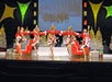 Girls dressed in red and white dance with sleighs and presents in the background