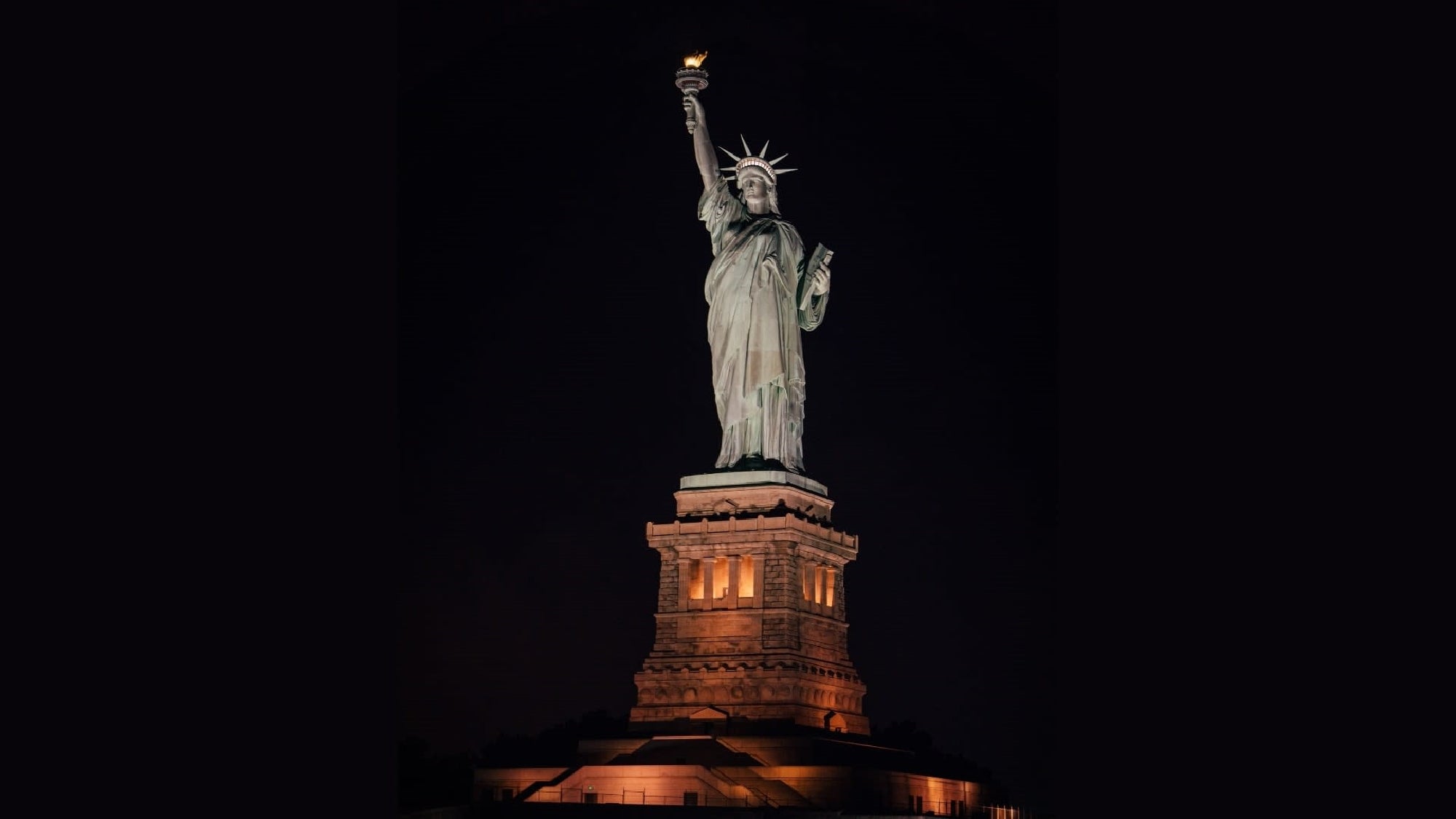 The Statue of Liberty is illuminated at night, standing on its pedestal against a dark sky.