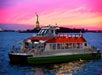 A ferry sails on the water near the Statue of Liberty at sunset, with a vibrant pink and orange sky in the background.