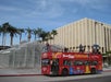A red double-decker StarLine City Sightseeing bus is parked near outdoor streetlamp sculptures and palm trees at a city intersection.