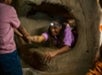 A child helps another child climb out of a large, hollowed rock structure indoors.